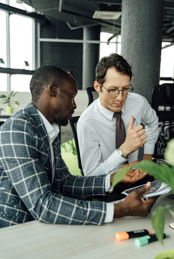 why-choose-us Two businessmen discussing work at a desk in a contemporary office setting.